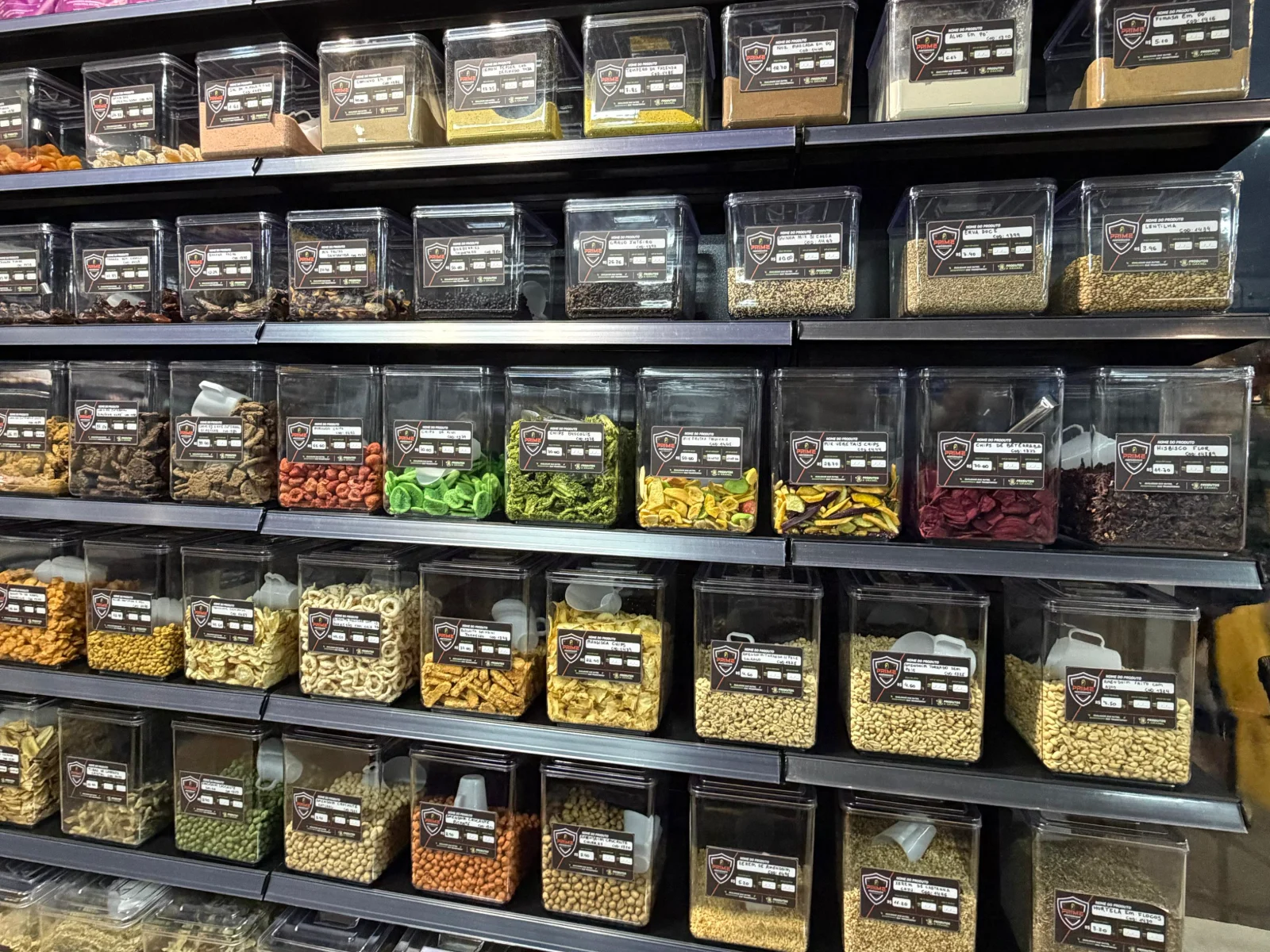 Parede de dispensers de produtos a granel na loja Prime Performance em Campo Grande MS, com castanhas, sementes, grãos, cereais, granolas, farinhas e chás