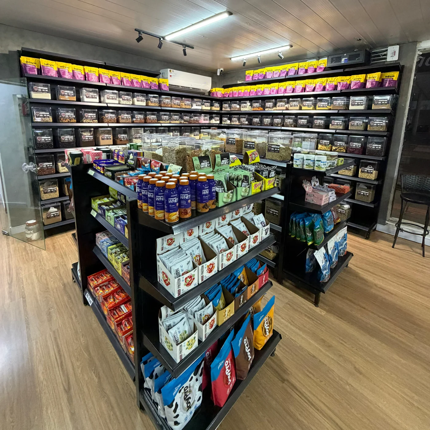 Interior da loja Prime Performance Suplementos em Campo Grande MS, com parede de dispensers de produtos a granel e gôndola central de suplementos